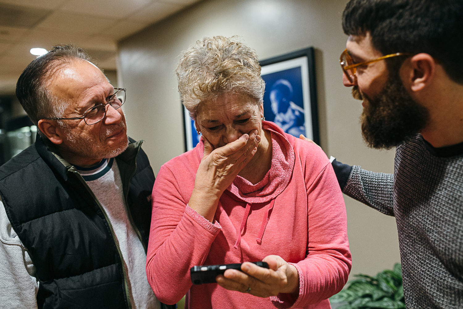two grand parents one covering her mouth in shock looking at a picture of new grandson