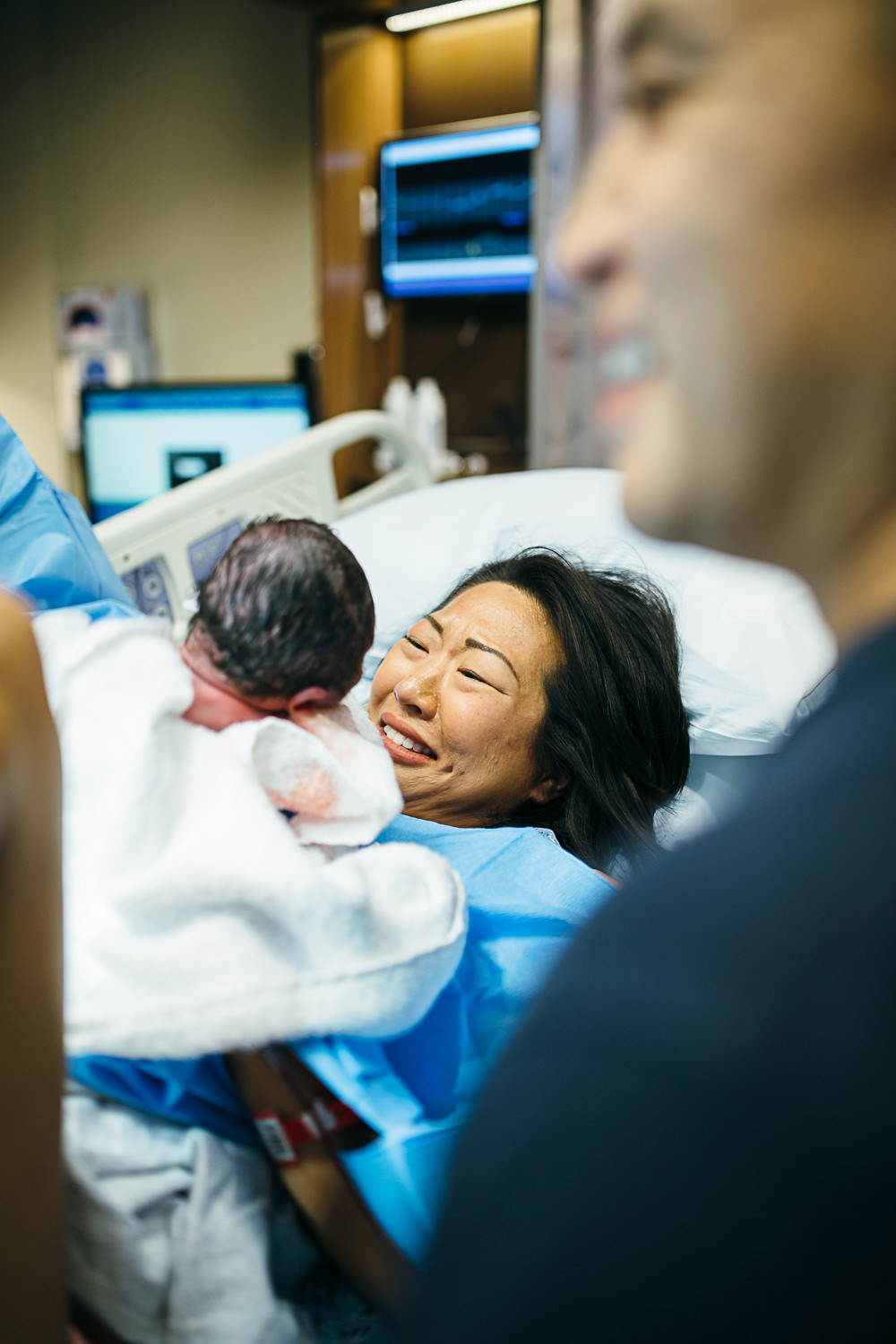 asian mother looks and newborn son while laying in a hospital baby just after delivery