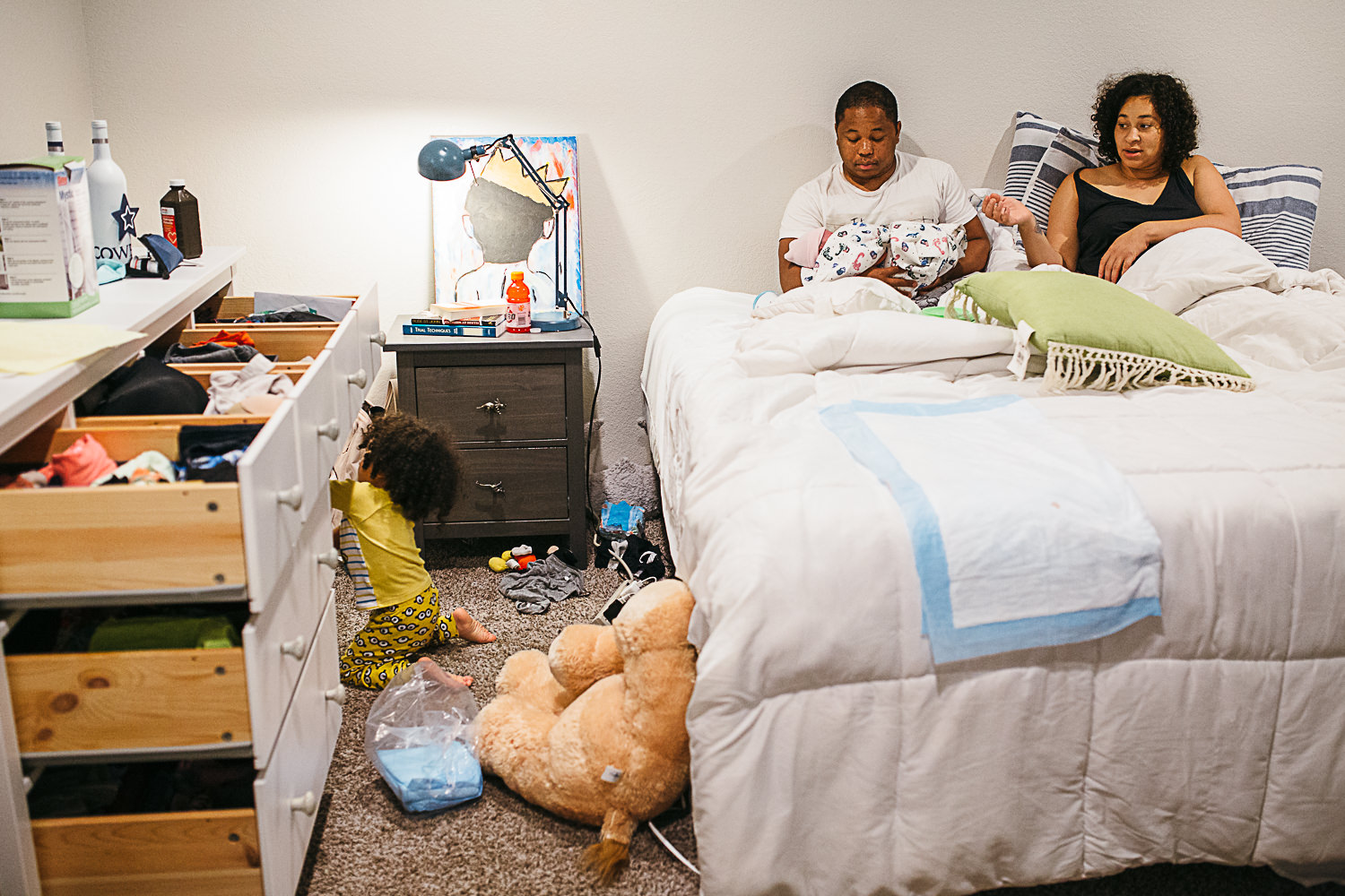 two parents sit in bed while their toddler makes a mess