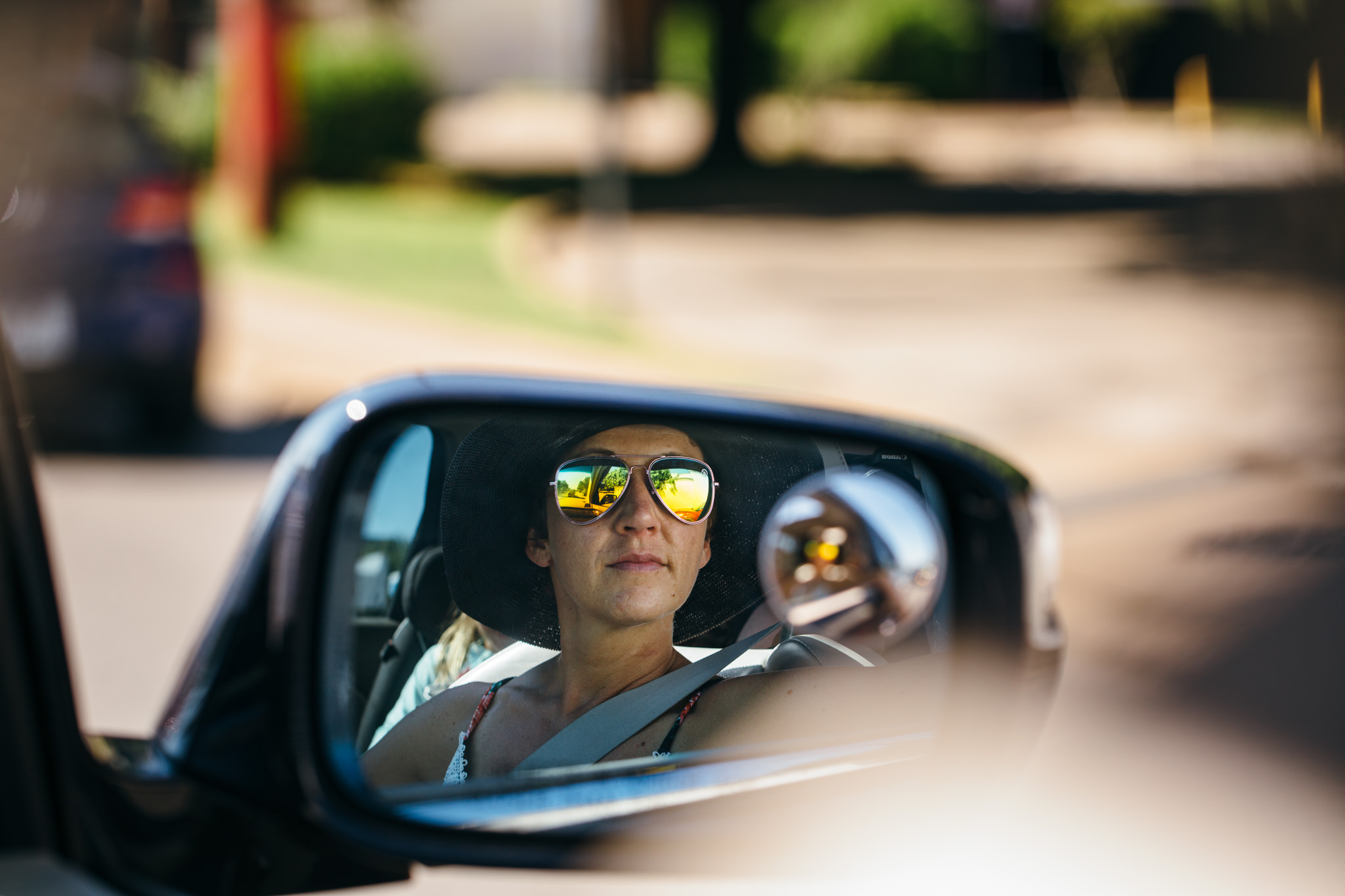 Woman wearing sunglasses in rearview mirror